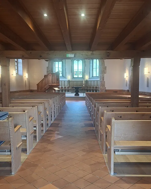 Innenraum der reformierten Kirche Vechigen mit Holzbänken und Altar.