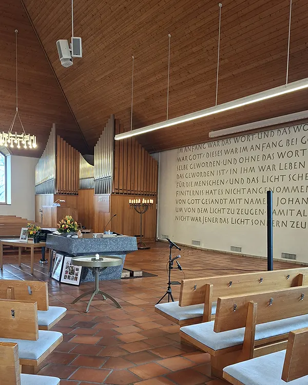 Innenraum der reformierten Kirche Opfikon mit kreisförmig angeordneten Sitzbänken, Steinaltar und Orgel während der Vorbereitung einer Trauerfeier.