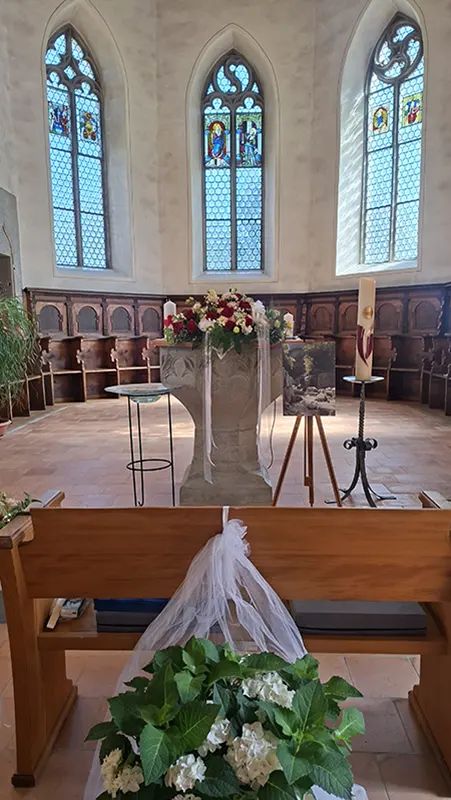 Altarbereich der Kirche Seeberg mit Blumen, Kerze und drei Kirchenfenstern
