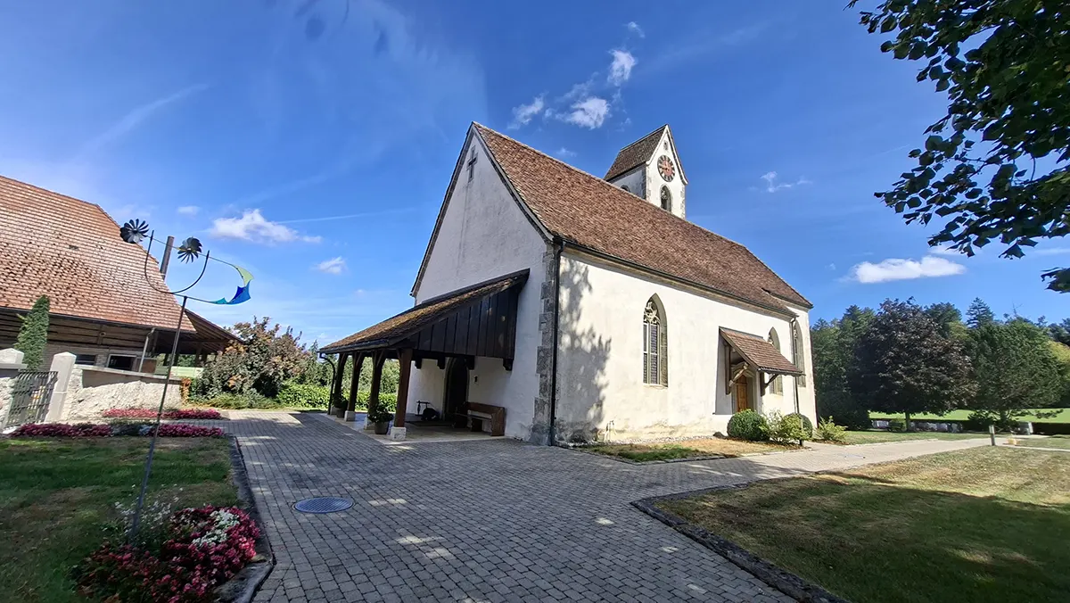 Kleine Kirche Seeberg mit weissem Mauerwerk und rotem Ziegeldach bei blauem Himmel